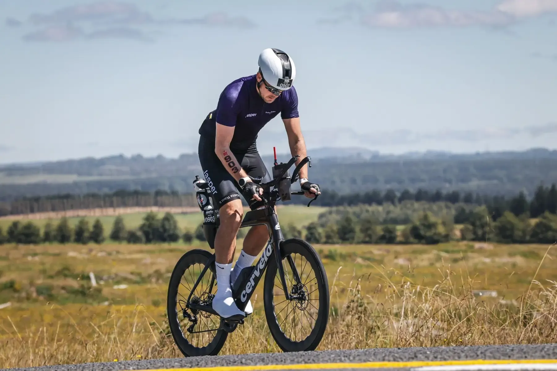 A triathlete on a time trial bike on an open country road with hills behind